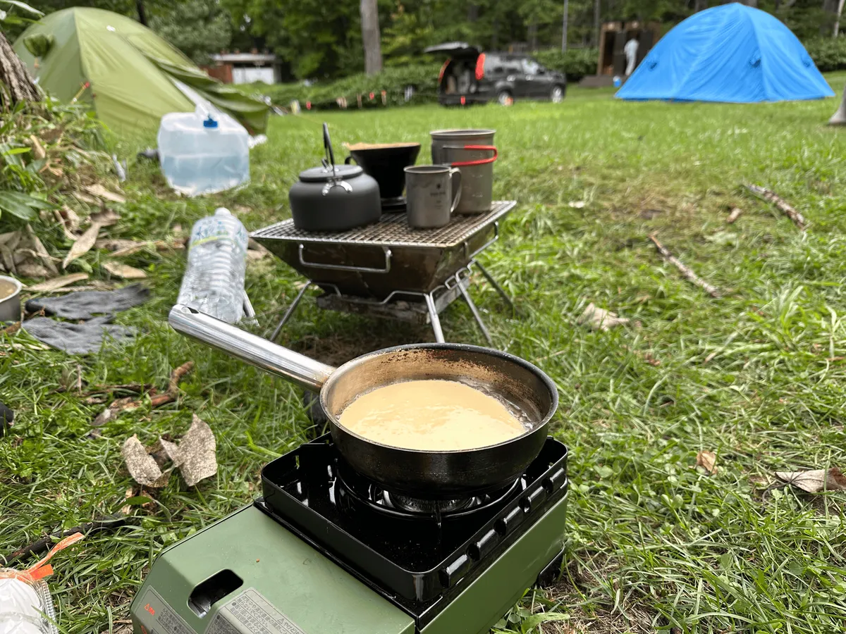 "A pancake being cooked on a portable stove. There is ca drip coffee setup in the background"